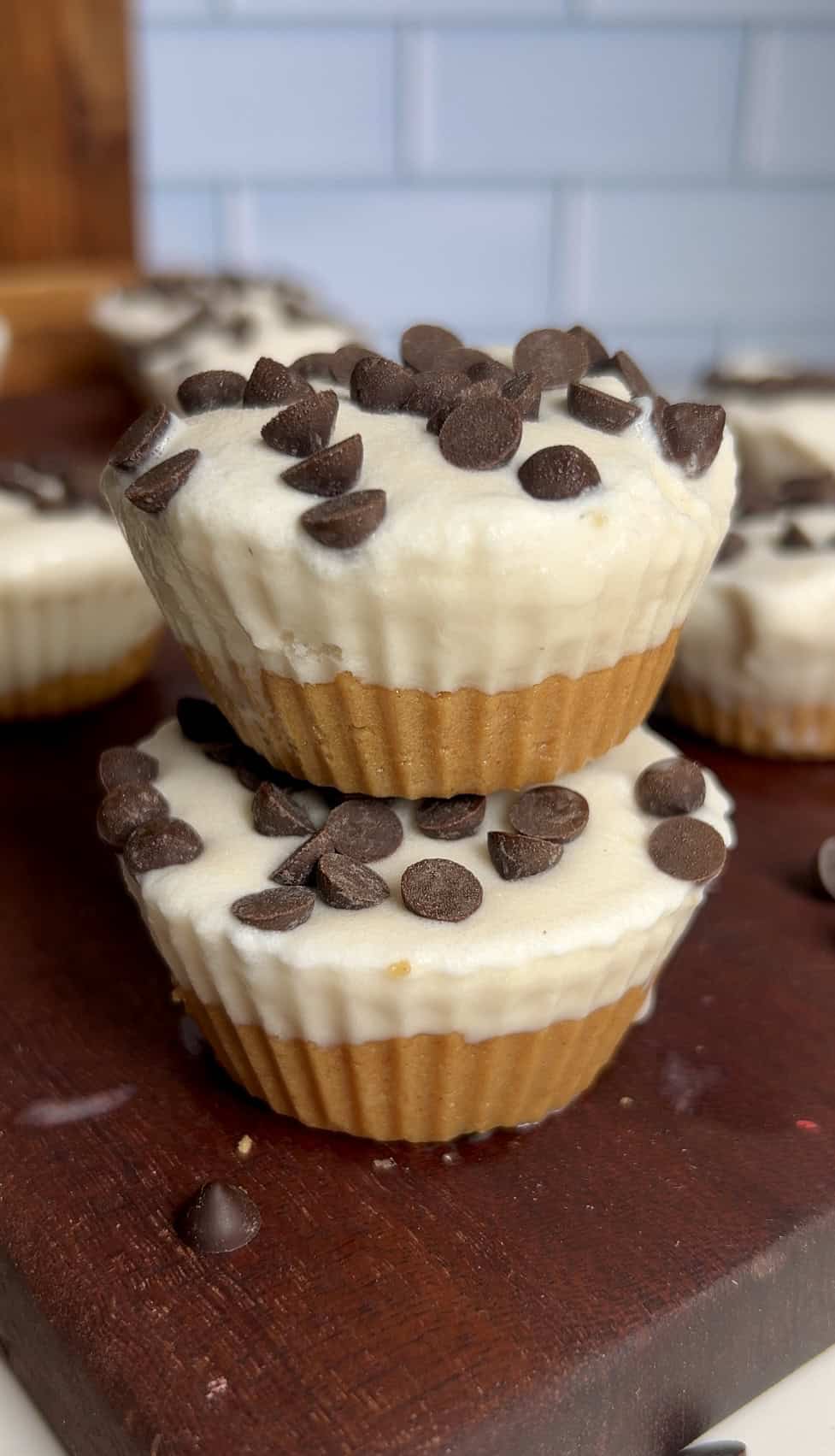 Two stacked cookie dough ice cream cups topped with mini chocolate chips on a wooden board with more cups in the background.