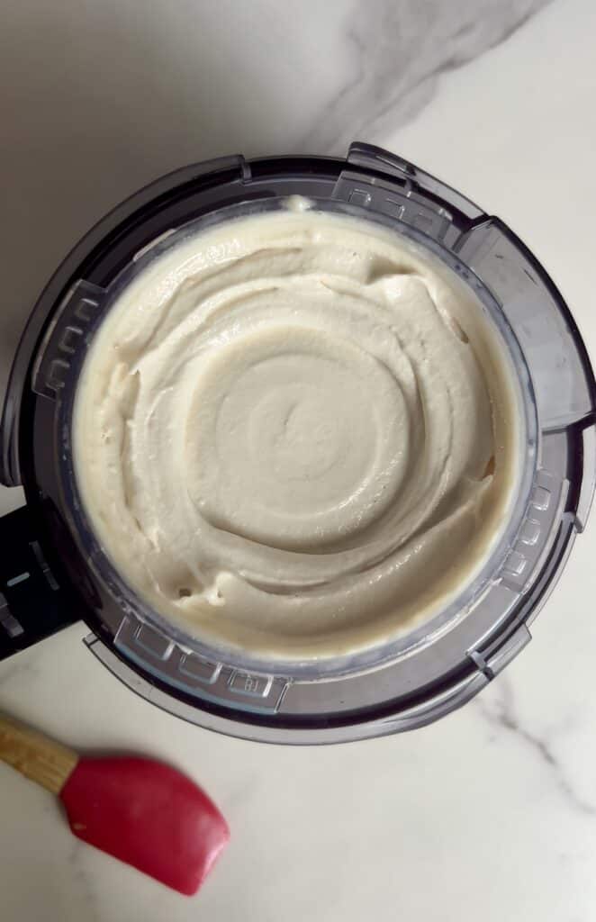 Creamy vanilla protein ice cream mixture freshly blended in a Ninja Creami container with a red spatula beside it.
