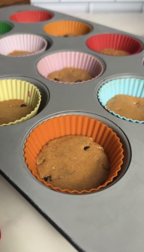 Pressed cookie dough layer set in silicone muffin liners inside a baking tray, ready for the ice cream topping
