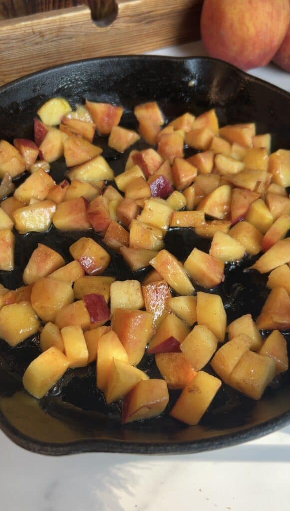 Caramelized diced peaches cooking in a cast‑iron skillet for high‑protein peach cobbler ice cream