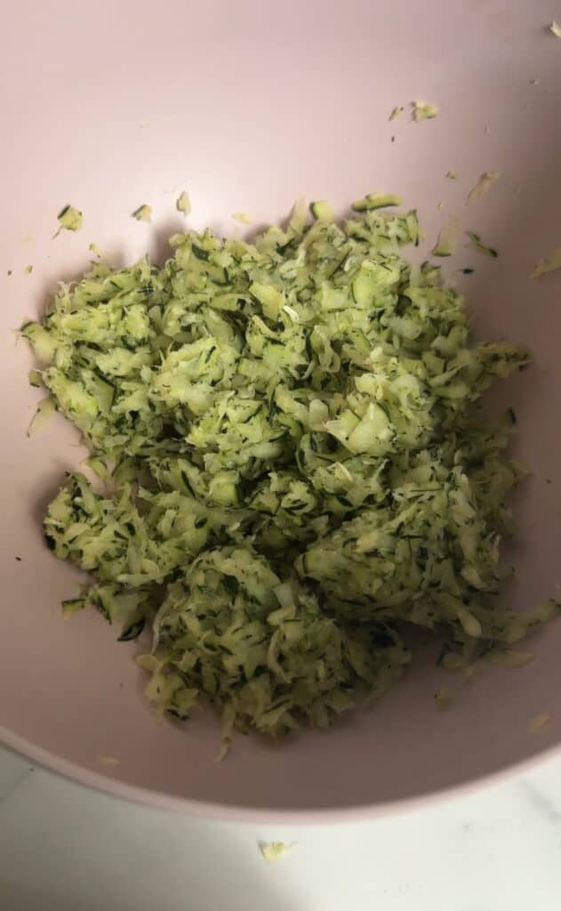 Finely grated zucchini in a pink mixing bowl, ready to be used in healthy gluten‑free blondie batter.