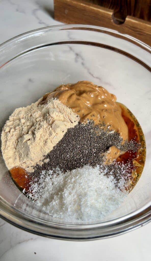 Mixing bowl filled with peanut butter, honey, protein powder, chia seeds, and shredded coconut before stirring — ingredients for high‑protein PB&J energy bites.