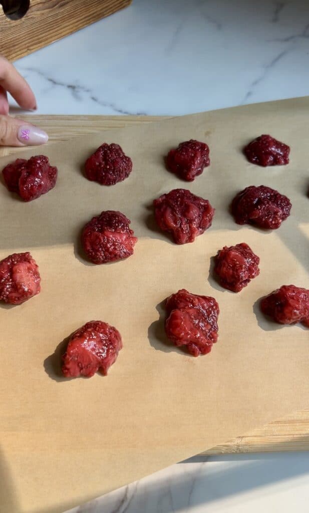 Dollops of homemade strawberry chia jam arranged on parchment paper, ready to freeze for stuffing inside PB&J protein energy bites