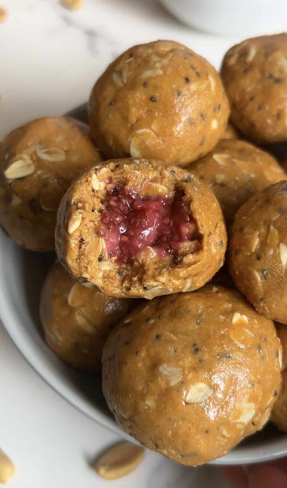 Close‑up of a peanut butter oat energy bite with a bite taken out, revealing a gooey strawberry chia jam center surrounded by oats and chia seeds.