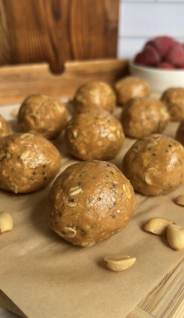 Peanut butter oat energy bites arranged on parchment paper with scattered peanuts and a bowl of strawberries in the background — no‑bake protein snack.