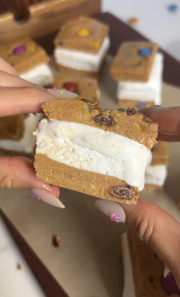 Hands holding assembled ice cream sandwich with remaining sandwiches on parchment paper in the background