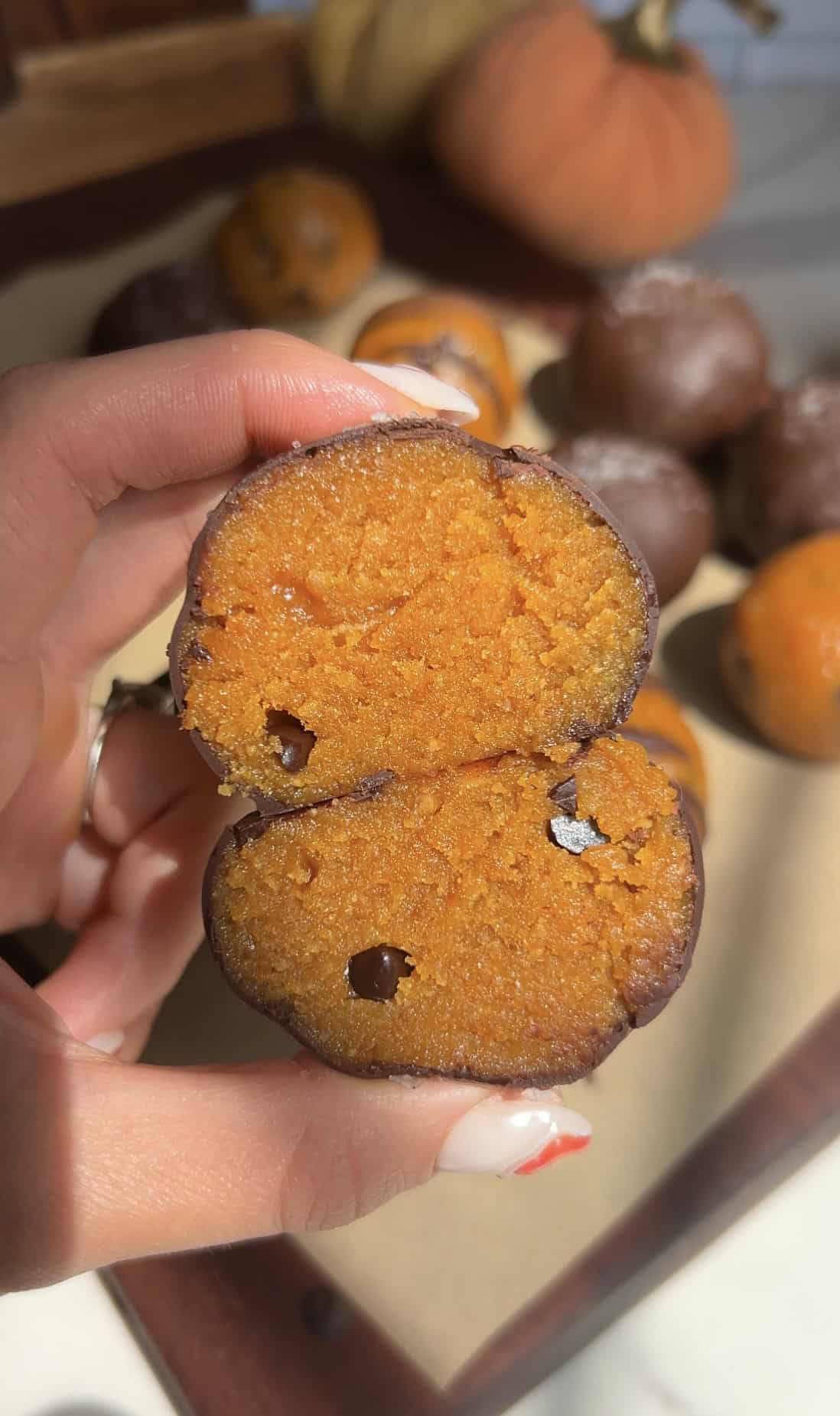 Close-up of a pumpkin cookie dough truffle cut in half showing orange interior.