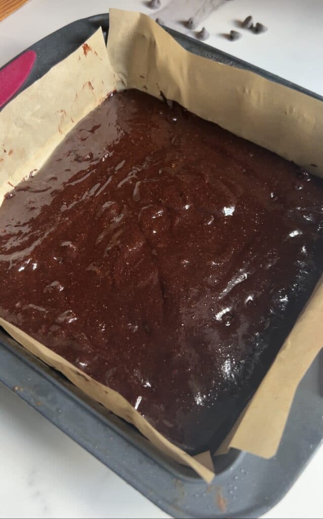 Raw Brownie batter in a baking pan with parchment paper.