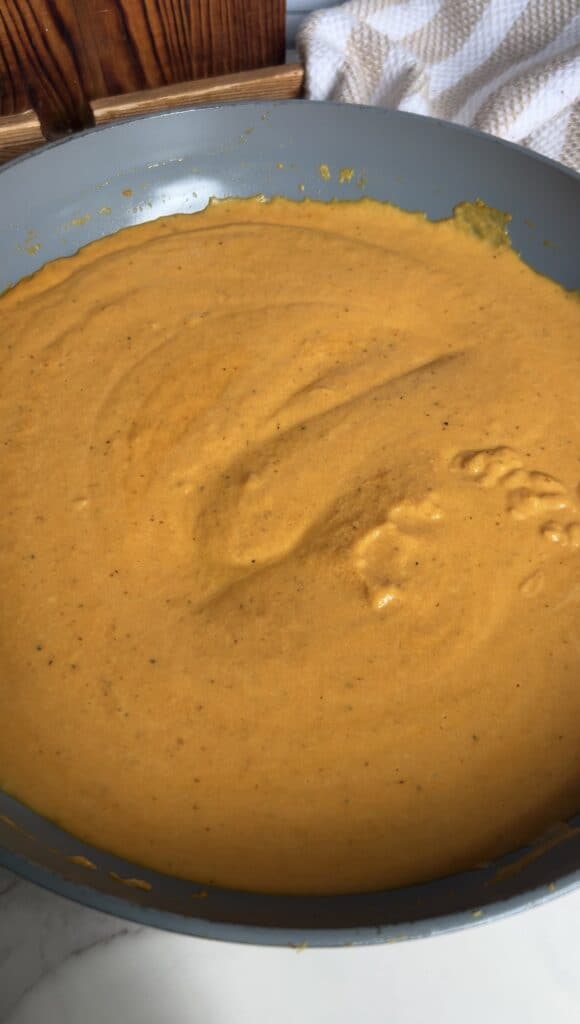 Smooth, orange pumpkin parmesan sauce in a skillet for ravioli to be tossed in