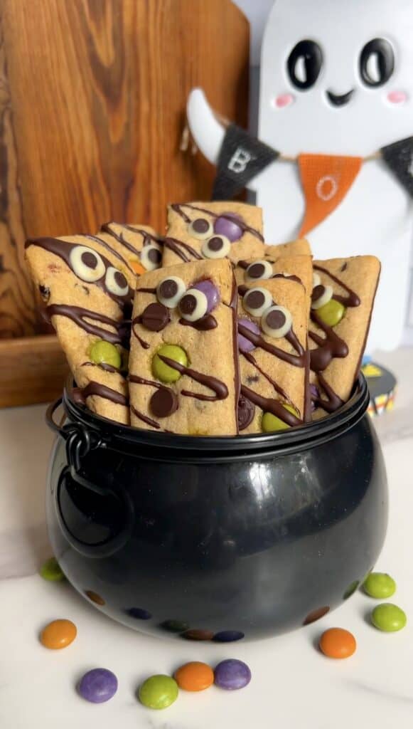 Colorful Halloween cookie fries with chocolate drizzle in a black cauldron.