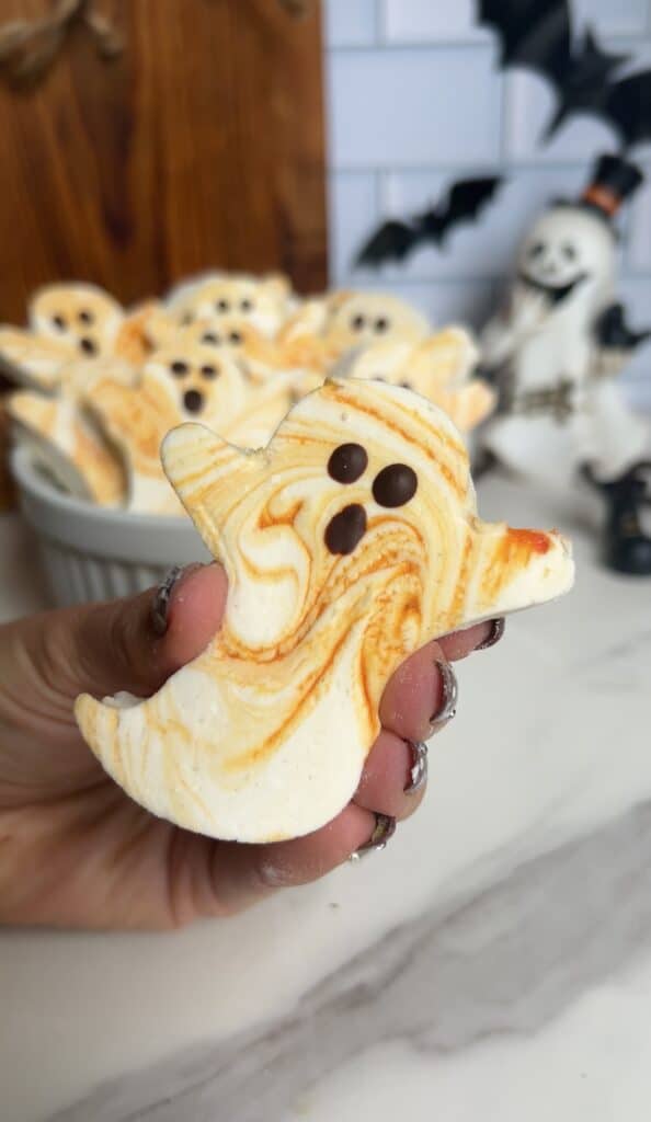 Ghost-shaped marshmallow treat with orange swirls and chocolate eyes and mouth.