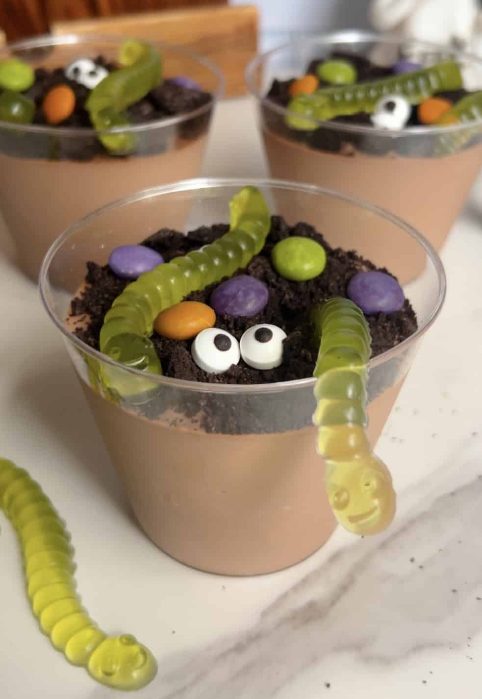 Halloween dirt cups with gummy worms and colorful candies in clear cups.