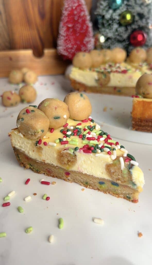 Slice of holiday sugar cookie cheesecake with sprinkles and cookie dough balls.