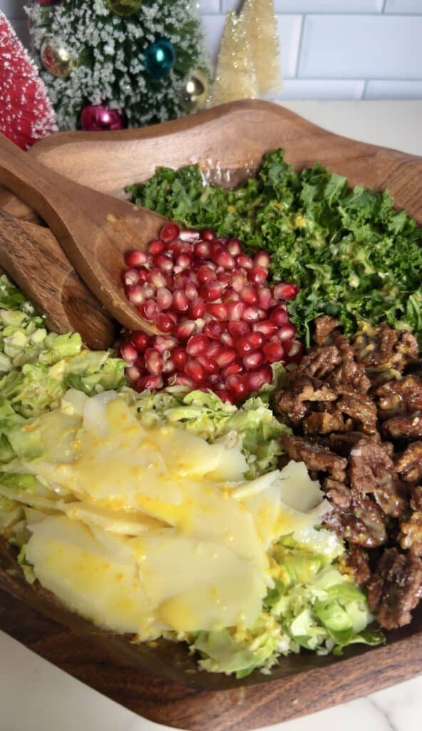 Fresh Brussels sprouts, kale, pomegranate, candied pecans, and cheese in a wooden bowl with homemade citrus dressing to top