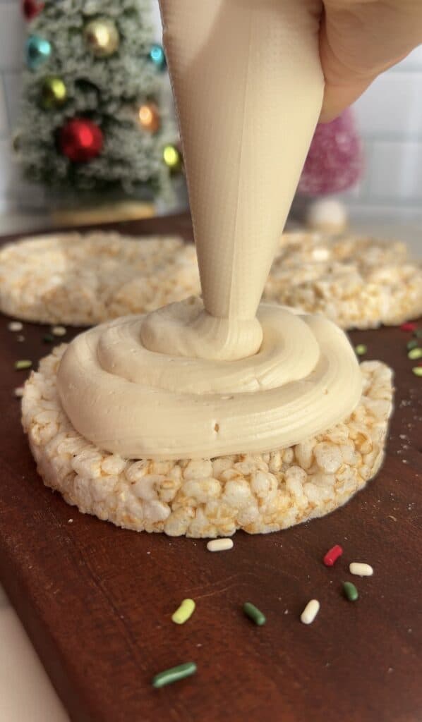 Creamy yogurt frosting being piped onto a rice cake treat with sprinkles.